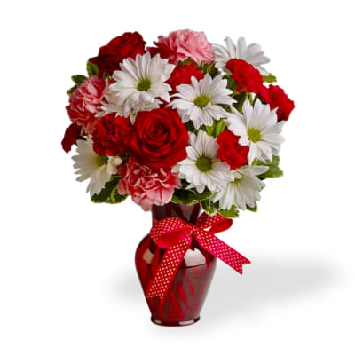 Red roses, white daisies, and pink carnations in a red vase with a polka-dot ribbon