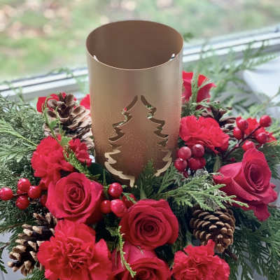 Red roses and carnations arranged around a gold candle holder with pinecones.