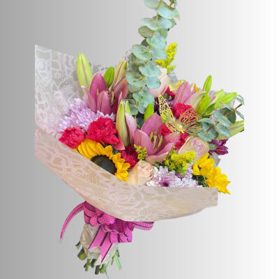 Mixed bouquet with pink lilies, sunflowers, carnations, and chrysanthemums wrapped in patterned paper
