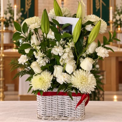 White floral arrangement in a wicker basket with a red ribbon