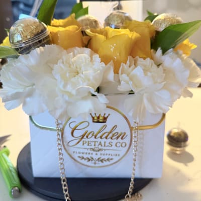 White carnations and yellow roses in a branded gift box with chocolates