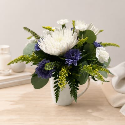 White and purple flowers arranged in a white mug vase