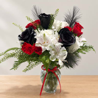 Bouquet of red, white, and black flowers in a glass vase with a red ribbon