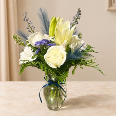 White and pale yellow flowers in a glass vase with a blue ribbon