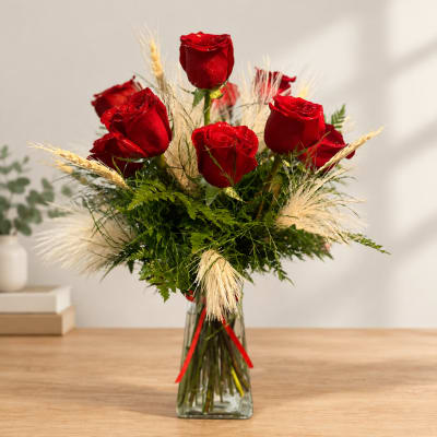 Red roses arranged in a clear glass vase with dried grass accents