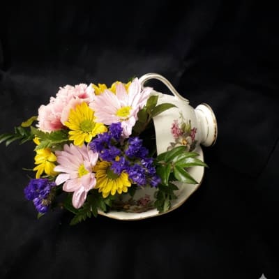 Mixed pink, yellow, and purple flowers arranged in a floral teacup