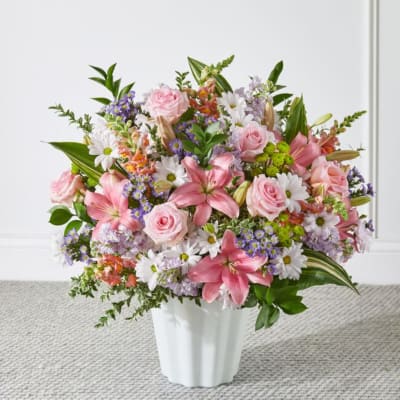 Pink roses and lilies arranged with white daisies in a white vase