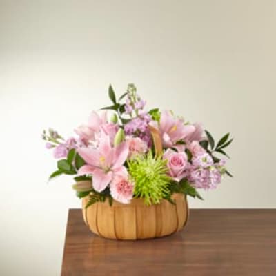 Pink and lavender flower arrangement in a wooden basket on a table