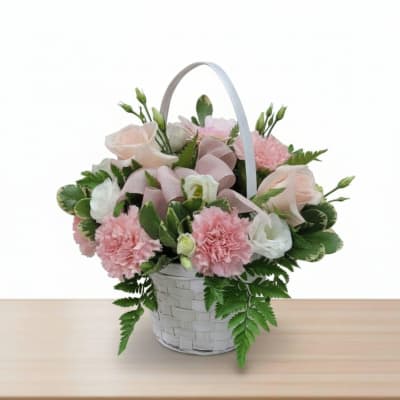 Pink and white flowers arranged in a white basket with a ribbon handle