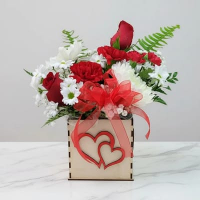 Red and white flower arrangement in a wooden box with a red ribbon