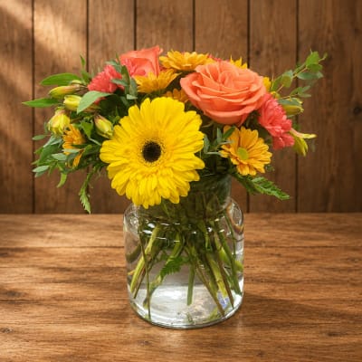 Bouquet of yellow daisies, coral roses, and pink carnations in a glass vase