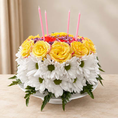 Round floral cake with yellow roses, white daisies, and pink candles