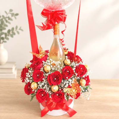 Red rose arrangement around a champagne bottle with ribbons and balloons