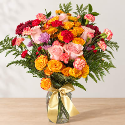 Bouquet of pink, yellow, and red flowers in a glass vase with a gold ribbon