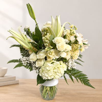 White floral arrangement with lilies, roses, and hydrangeas in a glass vase