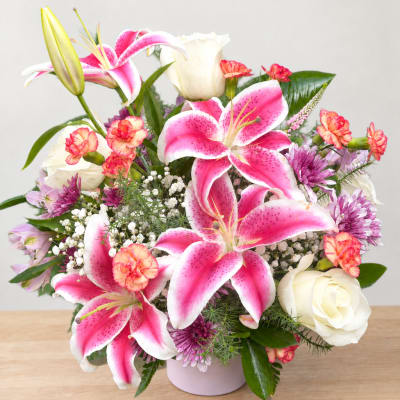 Pink lilies and white roses arranged in a pale vase