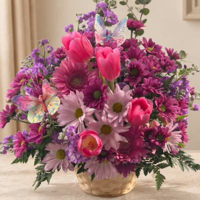 Pink and purple mixed flower arrangement in a woven basket with butterfly picks