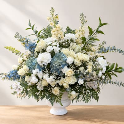Large white and cream floral arrangement in a white vase with blue accents