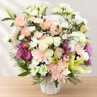 Mixed pastel bouquet in a white vase with roses, lilies, and daisies