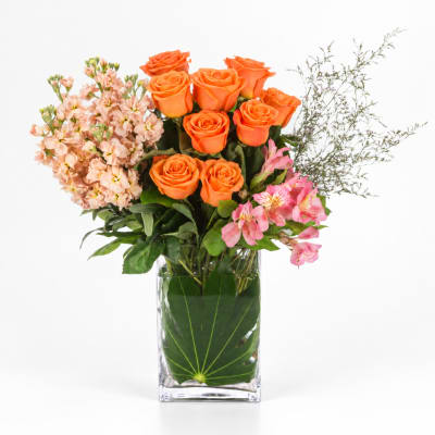 Orange roses with pink flowers in a clear glass vase