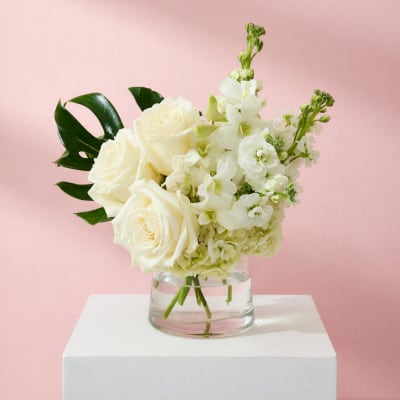 White roses and white flowers in a clear glass vase on a white pedestal