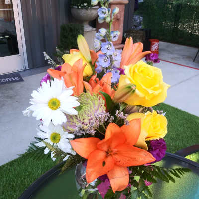 Bright mixed bouquet with lilies, roses, daisies, and purple accents in a glass vase