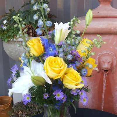 Yellow and white roses with blue and purple flowers in a glass vase