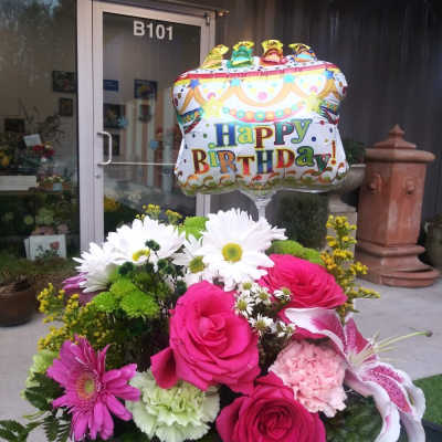 Birthday balloon above a colorful flower arrangement in a basket