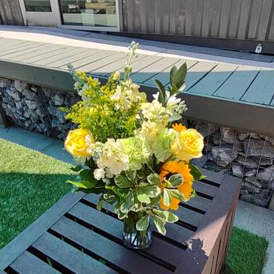 Yellow roses and white flowers arranged in a glass vase