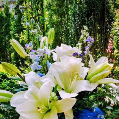 White lilies and blue flowers arranged with a blue ribbon