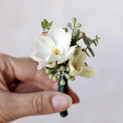 White boutonniere with small green accents held in a hand