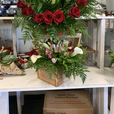Two floral arrangements with red roses, lilies, and calla lilies in wooden boxes