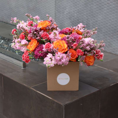 Pink and orange mixed flower arrangement in a brown box