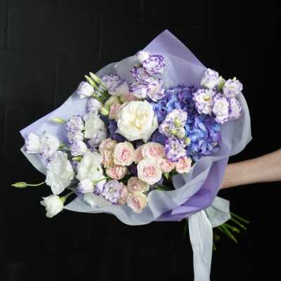 Hand-tied bouquet of purple, white, and pink flowers wrapped in lavender paper
