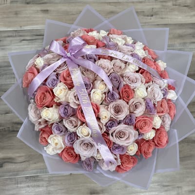 Round bouquet of pink, lavender, and white roses with a lavender ribbon