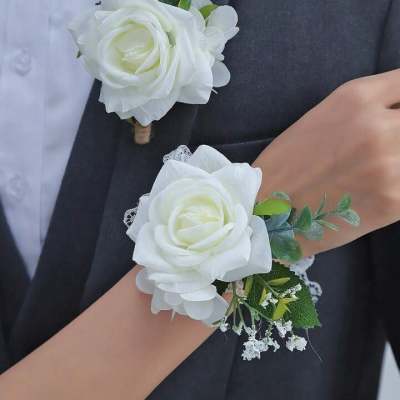 Matching white rose boutonniere and wrist corsage with small white filler flowers on formal attire.