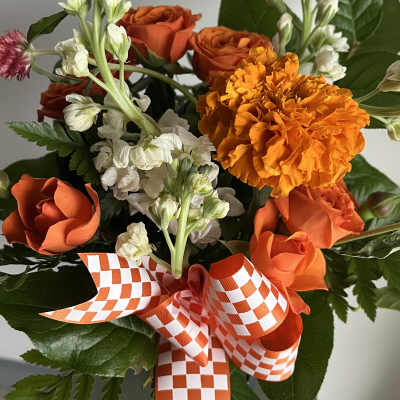Orange roses and marigold bouquet with white flowers and checkered ribbon