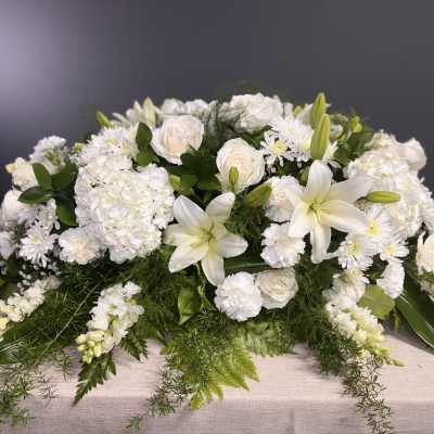 White floral casket spray with lilies, roses, and chrysanthemums