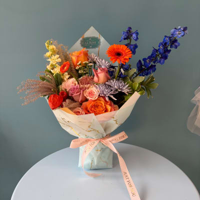 Mixed bouquet of roses, gerberas, and blue delphinium in wrapped paper