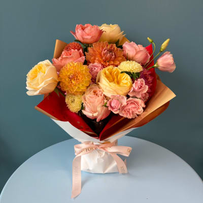 Mixed bouquet of pink, yellow, and peach flowers wrapped in paper