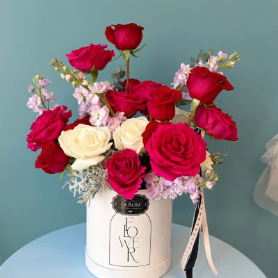 Red and white roses arranged in a white hat box with pink filler flowers