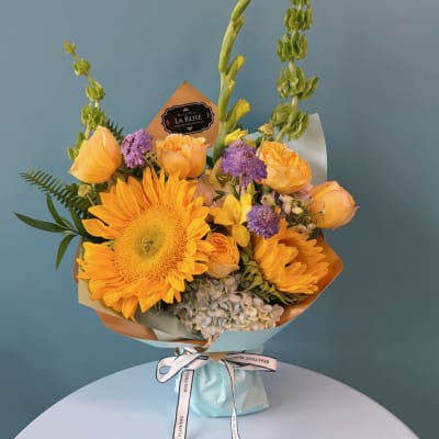 Bouquet of yellow sunflowers and roses with purple accents in pastel wrapping
