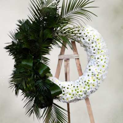 Large floral wreath with white flowers and dark palm fronds on an easel