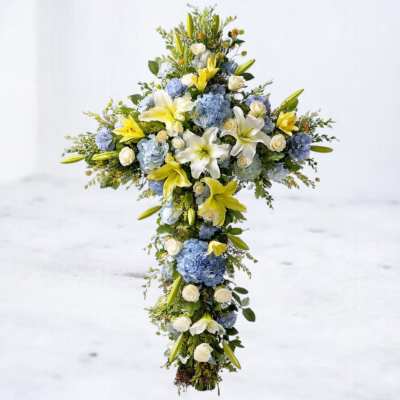Tall floral cross with white lilies, blue hydrangeas, and white roses
