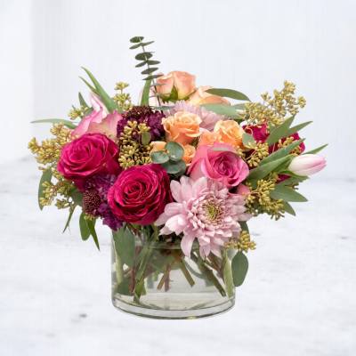 Mixed pink and peach flowers arranged in a clear glass vase