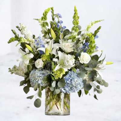 White lilies and roses with blue hydrangeas in a glass vase