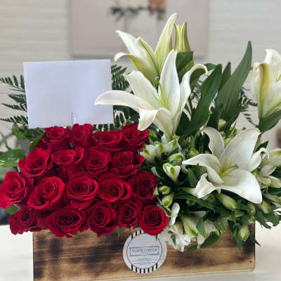 Red roses and white lilies arranged in a wooden box with a blank card