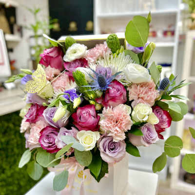 Pink, white, and lavender rose and carnation arrangement in a white box with ribbon and butterfly accent