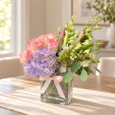 Pink roses and lavender hydrangea in a glass vase with a ribbon