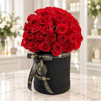 Red roses arranged in a black round box with a gold ribbon